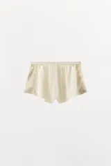 Shorts de tiro alto confeccionado en tejido satinado color verde oliva, con cintura elástica, bajo con volantes y aberturas laterales decoradas con aplicaciones de encaje a tono.