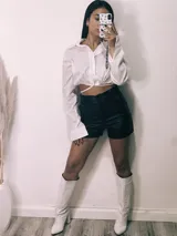 Camisa cropped negra con cuello clásico, mangas largas con puños abotonados y cierre frontal con botones. Presenta detalle de tachas plateadas en el cuello.