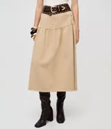 Pollera midi color beige confeccionada en sarga de algodón certificado BCI, con cintura alta y pasadores, bolsillos frontales, recorte en la cadera con frunces y cierre de botón y cremallera.