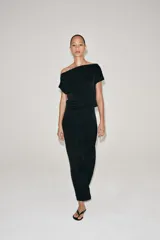 Vestido midi negro confeccionado en hilatura de viscosa, de diseño satinado y corte asimétrico con escote fluido y manga sisa. Presenta bajo acabado en línea evasé y cierre lateral con cremallera oculta en costura.