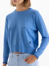 Sweater de tejido de punto en color gris, con cuello redondo, mangas largas y detalle de bordado amarillo en el puño y en el lateral inferior. Presenta un corte recto y estructura ligera.