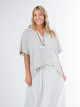 Blusa tipo poncho confeccionada en lino italiano color gris claro, con escote en V y calce amplio.