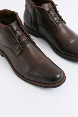 Botas de cuero color marrón con cordones, diseño de puntera reforzada y suela de goma con detalle de costura.