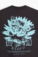 Remera de algodón negra, de corte holgado y diseño de hombros caídos. Presenta un pequeño estampado en el pecho con una flor celeste y el texto "KEEP THE WILD ALIVE".