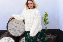 Sweater artesanal de tejido de punto de lana merino color marfil, de calce amplio y relajado, con cuello redondo y diseño frontal en relieve con trenzas y bodoques. Presenta mangas largas abullonadas con paneles texturizados y puños acanalados.