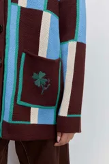 Cardigan de punto con diseño de bloques de color en azul, rojo y crema. Presenta cuello en V, cierre frontal con botones, mangas largas y dos bolsillos delanteros con bordado de cerezas.