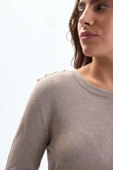 Buzo de punto color beige, con cuello redondo, manga larga y botones decorativos en los hombros y puños.