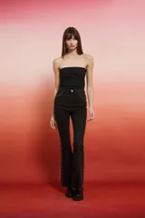 Pantalón jean negro de tiro alto, corte flare con tajo en el ruedo y detalles de tachas metálicas a los costados.