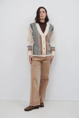 Saco tejido de punto con calce amplio, diseño de cuello en V y cierre frontal con botones. Presenta un patrón geométrico en tonos beige, marrón y detalles en azul brillante.