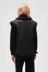 Chaleco de estilo aviador en color marrón, confeccionado en material tipo cuero con interior y bordes de corderito sintético en color crema. Presenta cierre frontal, cuello alto con tira de ajuste y bolsillos laterales.