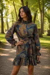 Vestido corto de lino con estampado abstracto en tonos tierra, azul y verde. Presenta cuello alto con volado, mangas largas con puños fruncidos, cintura entallada con lazo removible y falda con volado en el ruedo.