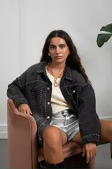 Campera de jean oversize color negro con diseño de tachas metálicas plateadas distribuidas en el cuello, hombros, frente y mangas. Posee cierre frontal con botones metálicos y bolsillos en el pecho.