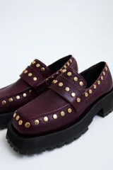 Mocasines de cuero color marrón con suela track negra y tachas doradas.