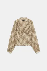 Camisa de manga larga con escote en V y cierre frontal con botones. Presenta un estampado de cuadros en tonos beige y marrón, con detalles de pliegues en el delantero y puños ajustados.