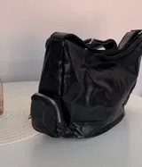 Cartera tipo hobo de cuero sintético color negro, con diseño espacioso y dos bolsillos laterales estilo cargo con cierre. Incluye correa ajustable para el hombro y bolsillo interno.