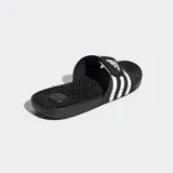Ojotas Adidas Adissage negras con tres franjas blancas en la tira superior ajustable con velcro. La plantilla cuenta con protuberancias de masaje EVA.