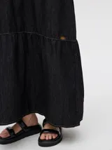 Vestido midi de denim color marrón, con corte holgado, breteles finos con lazos ajustables y detalle de volado en el ruedo.