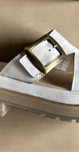 Sandalias de cuero natural blanco modelo Rina, con leve plataforma y suela dentada. Presentan una tira ancha cruzada con detalle pintado a mano multicolor y una hebilla metálica personalizada en tono oro viejo.