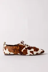 Zapato tipo flat de estilo acordonado, confeccionado en cuero con pelo con estampado de manchas tipo vaca en tonos marrón y blanco.