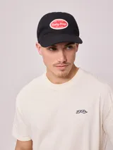 Gorra de lona lavada color beige con visera azul marino y parche bordado con el logo de Rusty.