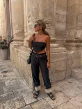 Pantalón negro de tiro alto con cintura elástica fruncida, corte holgado y detalle de puntilla blanca en los tobillos.
