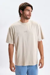 Remera de manga corta con corte oversize, color beige, con cuello redondo y estampado sutil en el centro del pecho.