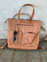 Mochila de cuero marrón con cierre superior y múltiples bolsillos externos. Se puede convertir en bolso de mano o bandolera gracias a sus correas ajustables y extraíbles.