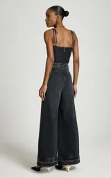 Jean wide leg negro de tiro alto con perneras anchas y dobladillo deshilachado, con bolsillos delanteros y traseros, y cierre frontal con botón metálico y cremallera.