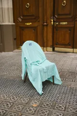 Bata de lino con diseño de rayas verticales en color turquesa y blanco. Presenta un corte holgado, mangas largas y un lazo ajustable en la cintura. Incluye un pequeño parche con el logo de la marca en la parte superior trasera.