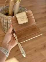 Billetera de cuero dorada con textura croco, cierre con broche y correa de muñeca.