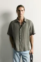 Camisa regular fit confeccionada en tejido de lino, color blanco, con cuello solapa, manga corta y cierre frontal de botonadura.