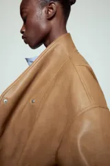 Chaqueta bomber ZW Collection confeccionada en tejido efecto piel de color marrón. Cuenta con cuello subido, manga larga con puño y botón a presión, bolsillos delanteros y bajo recto elástico. Cierre frontal cruzado con botones a presión.