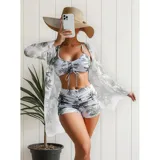 Conjunto de traje de baño de tres piezas con estampado de hojas tropicales en tonos blanco y negro. Incluye un top tipo tankini con cordón ajustable en el centro, un short de tiro alto y una camisa abierta de manga larga tipo salida de baño.