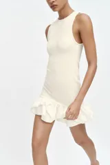 Vestido corto de color blanco con cuello redondo y diseño sin mangas. Presenta un cuerpo de tejido bouclé texturizado y un bajo acabado con volantes de tejido ligero.