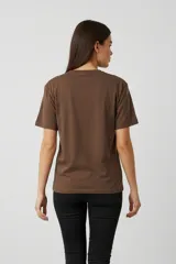 Remera de algodón color marrón con cuello redondo y mangas cortas. Presenta un estampado frontal con ilustraciones de dos copas de cóctel decoradas con lazos.