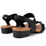 Sandalia de cuero negra con elástico en el tobillo, taco bajo y hebilla decorativa.