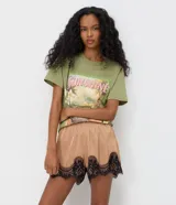Short de satén color beige con acabado brillante, corte holgado, cintura elástica y detalle de encaje floral negro en el bajo.