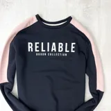 Buzo negro con mangas color rosa pálido y texto estampado en blanco que dice 'Reliable Duxon Collection'.