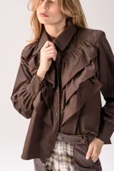 Camisa blanca de corte clásico con volados frontales y en los hombros, manga larga con puños abotonados y cierre frontal con botones.