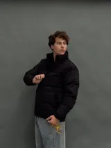 Campera puffer negra con diseño de paneles, cierre frontal completo y cuello alto. Presenta una textura diferenciada en la parte superior y bolsillos laterales.
