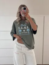 Remera oversize marrón con estampado gráfico frontal en tonos celestes y blancos con la leyenda "Only Fans", palmeras y estrellas.