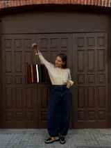 Cartera tipo tote de cuero con diseño de franjas verticales multicolores en tonos tierra, rojo y azul. Cuenta con correas trenzadas de cuero y cierre superior.