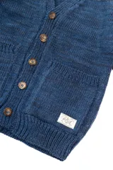 Cardigan azul de lana merino con cuello en V, cierre con botones marrones y dos bolsillos frontales.