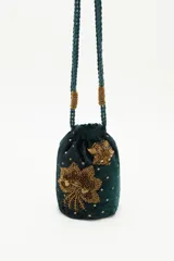 Cartera tipo bolso de mano color negro, confeccionada en terciopelo con bordados de estrellas y aplicaciones de pedrería brillante. Cuenta con correas trenzadas de cordón negro y cierre superior.