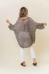 Buzo de tejido liviano y calado con brillo sutil, color gris oscuro o negro. Presenta un calce amplio y mangas amplias, con un detalle de tiras entrelazadas en la espalda. El largo es irregular, más largo en la parte trasera.