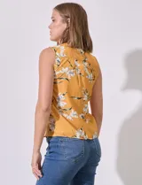 Blusa amarilla sin mangas de satén estampado con flores blancas. Tiene cuello a la base y escote en V.