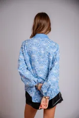 Camisa de manga larga con diseño abullonado, confeccionada en tela bordada con motivos florales. Presenta cierre frontal con botones y puños elásticos.