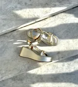 Sandalias de plataforma doradas, con suela ancha y tiras anchas cruzadas en el empeine y una tira ajustable en el tobillo.