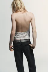 Top halter de tul color gris claro, con escote fluido drapeado y espalda descubierta. Presenta bordados con aplicación de abalorios en tonos oscuros y dorados.