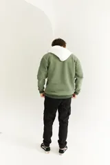 Canguro verde seco con capucha y cordones blancos, cierre parcial con cremallera, bolsillo tipo canguro y logo bordado en el pecho.